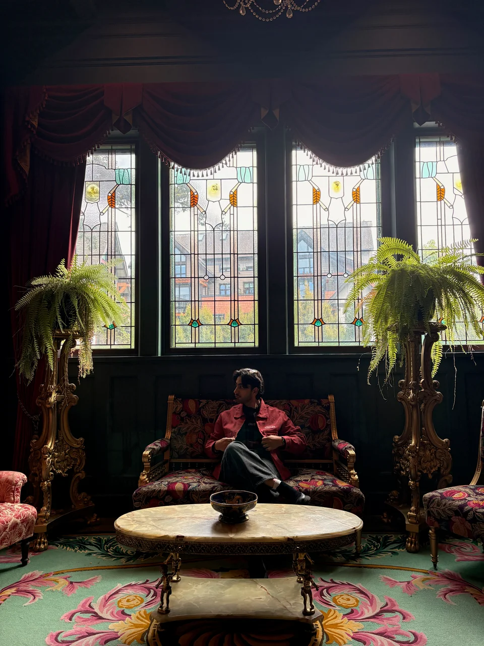 Seated portrait in a manor with stained-glass windows and plants